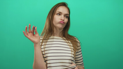 Fototapeta premium Young caucasian woman writing on notepad with blue pen in green studio wearing striped shirt; contemplation.