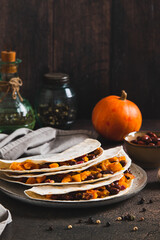 Delicious tacos with baked pumpkin, beans and cheese on a plate on the table vertical view