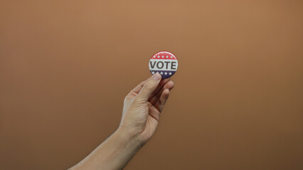 Man holding a political vote button against a brown wall, showcasing engagement and participation...