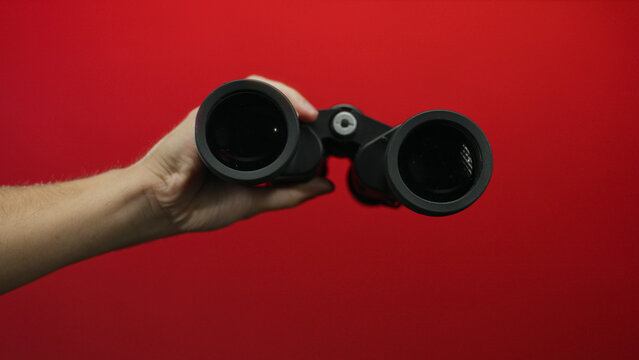 Man holding binoculars against a vibrant red background, highlighting the focus on exploration, technology, and observation in a striking composition of color and contrast.