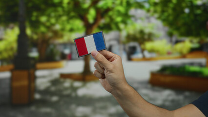 Man holding an embroidered french flag patch in a park, showcasing national pride amidst lush greenery and outdoor ambiance.