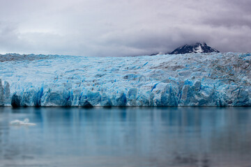 Massive blue glacier wall reflecting in the water under cloudy skies in Patagonia, Argentina.