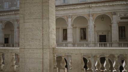 Stone balustrade and column in shallow focus at a historic building with arched cloister; background backdrop copyspace calm.