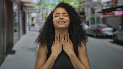 Woman distressed on urban street during daytime captures emotional intensity in public setting with curly hair and dark clothes reflecting worried expression amid blurred cityscape.