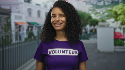 Smiling young woman volunteer in a purple shirt outdoors on a vibrant street illustrating community and youth engagement.