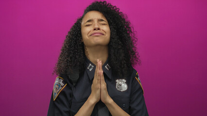 Woman police officer praying against vivid pink background in uniform showing emotions and faith...