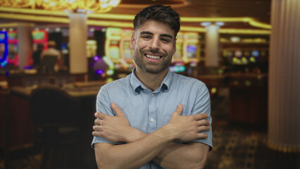Obraz premium Young hispanic man hugging chest beside glowing slot machine in brightly lit casino building; serenity.