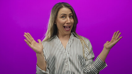 Middle age woman raises hands in studio with purple backdrop, mouth open in astonishment; surprise.