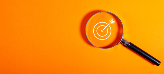 Magnifying glass with new year goals and target on orange background