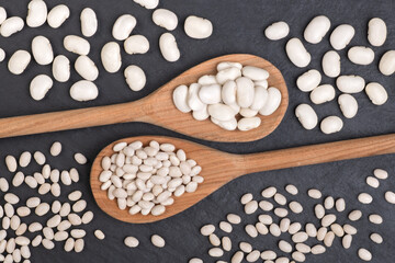 Wooden spoons with white beans on black backround, top view