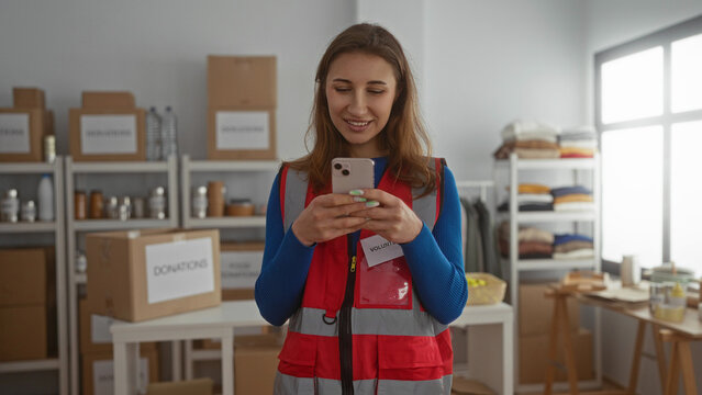 Young woman volunteer using phone in charity donations center room with boxes in the background showcasing a community support environment indoors.