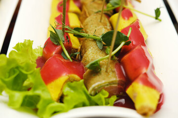 Colorful gourmet dish featuring rolled savory crepes topped with vibrant sauces and fresh herbs, elegantly arranged on a white plate with lettuce garnish, showcasing culinary artistry