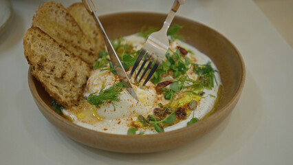 Delicious plated dish with yogurt topped with spices and herbs, served with grilled bread, highlighting a modern luxury dining experience indoors.