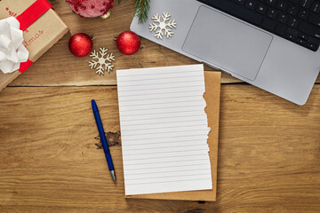 Top view wooden table with a blank sheet of paper, pen, laptop and gifts. Christmas gift list and...