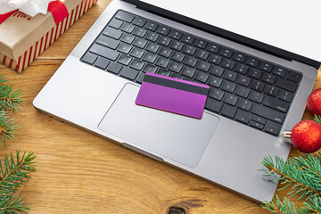 Credit card on laptop with Christmas decor on wooden desk. Concept of online shopping, secure payment, holiday sales and gift purchases
