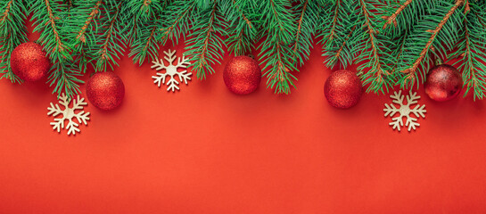Christmas evergreen branches with red glitter ornaments and wooden snowflakes on red background with copy space