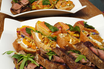 Gourmet open-faced sandwiches featuring smoked salmon, roast beef, fresh herbs, and vibrant vegetables arranged on elegant white platters, showcasing culinary artistry and presentation