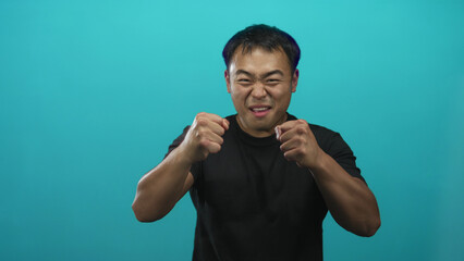 Young chinese man pointing finger and clenching fists in cyan studio setting; surprise...