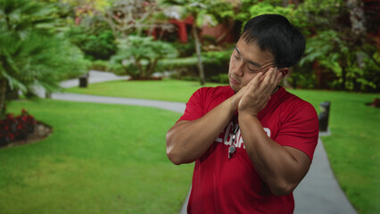 Young chinese lifeguard in red shirt resting head on hands on street; tiredness rest recovery fatigue.