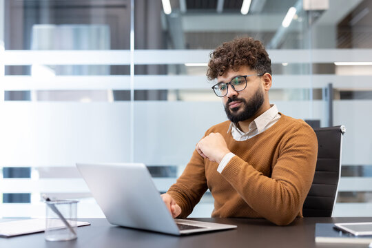 Young focused businessman working with a laptop at his desk in a blurred modern office environment, representing concentration, dedication, and professional productivity