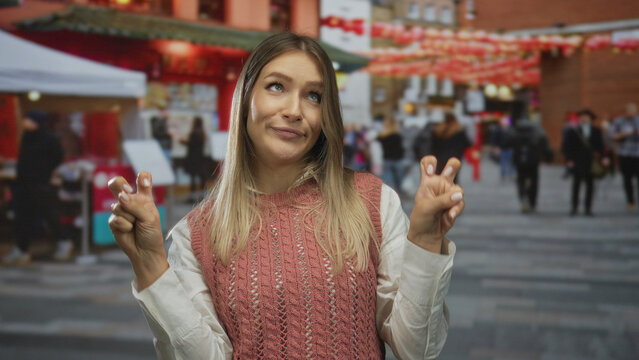 Woman smiling outdoors on busy city street gestures air quotes wearing casual outfit with vibrant urban backdrop enhancing lively atmosphere.