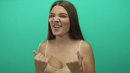 Teenage girl clenches fists while smiling broadly in mint green studio setting showcasing victory...