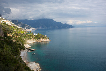 Fototapeta premium Gentle sunbeams pierce through a blanket of clouds, illuminating the calm sea and misty coastal mountains. The soft light creates a serene and ethereal atmosphere, highlighting the peaceful beauty