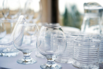 Clear glassware collection featuring elegant stemmed glasses and simple tumblers arranged on a table, showcasing transparency and reflections in a bright setting