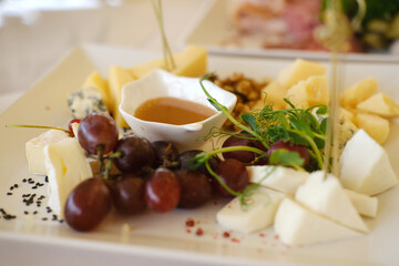 Elegant wedding appetizer platter featuring assorted cheeses, fresh grapes, and honey dip, beautifully arranged on a white plate for a sophisticated dining experience