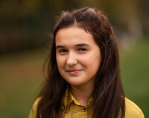 Fototapeta premium Portrait of a happy teenage girl in the autumn park, looking at the camera and smiling.