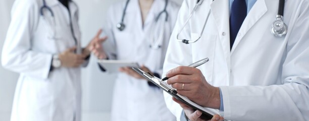 Doctor writing on a clipboard during a medical team discussion, collaborating on patient care,...
