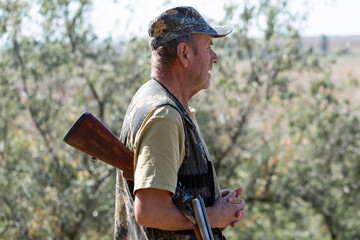 A hunter with a gun in camouflage clothing. A senior man with a gun, medium shot, searching for...