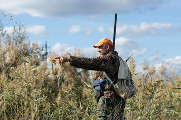 A hunter in camouflage clothing with a gun in his hands walks along the reeds.