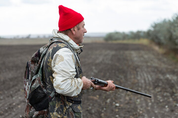 A hunter with a gun in camouflage clothing. A senior man with a gun, medium shot, searching for...