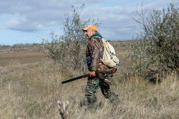 A hunter with a gun in camouflage clothing. A senior man with a gun, medium shot, searching for...