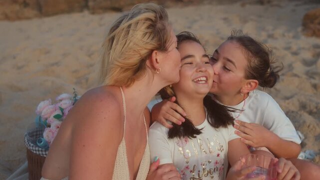 Mother and daughter kissing young girl on cheeks at sandy beach showing love, affection, family bonding during summer holiday