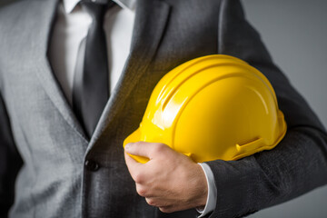 Business professional wearing a gray suit holding a yellow construction helmet symbolizing engineering management and safety leadership in industrial projects
