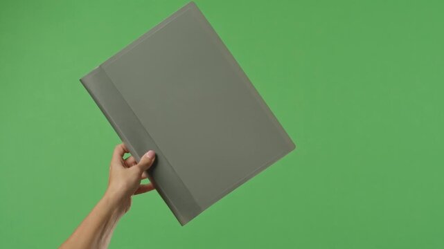 A woman hand holding a gray office folder with documents on a green chroma key background. Shot for designs related to office, business, education, and training.