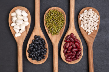 Beans selection in  spoons on black background, top view