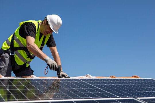 Workers install solar panels on a sunny day at a residential rooftop in an urban area