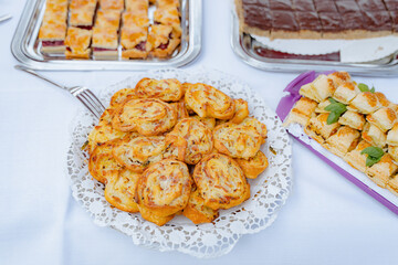 Close-up of baked appetizer swirls on a serving platter at a reception, flaky crust, cheese filling and nearby trays create a festive buffet scene ideal for food and hospitality concepts