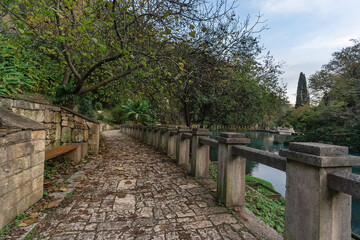 Scenic pathway lined with stone walls and lush greenery beside a tranquil water body