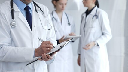 Doctor taking notes on clipboard during discussion with medical team involved in collaborative patient care, documentation, and health care strategy development in clinic