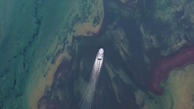 Aerial view of a blue hovercraft cruising above crystal water where vivid reefs and sand tongues are visible under the surface of Lake Lama. Topdown pace adds abstract beauty while keeping navigation