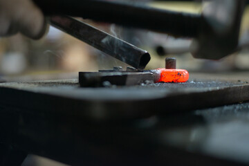 In the blacksmith's workshop, the blacksmith is leveling the red-hot metal with a hammer. A red-hot...