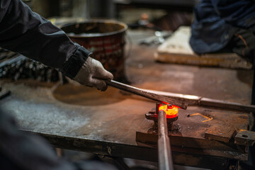 In the blacksmith's workshop, the blacksmith is leveling the red-hot metal with a hammer. A red-hot piece of metal with scale is being prepared for hardening. High quality photo