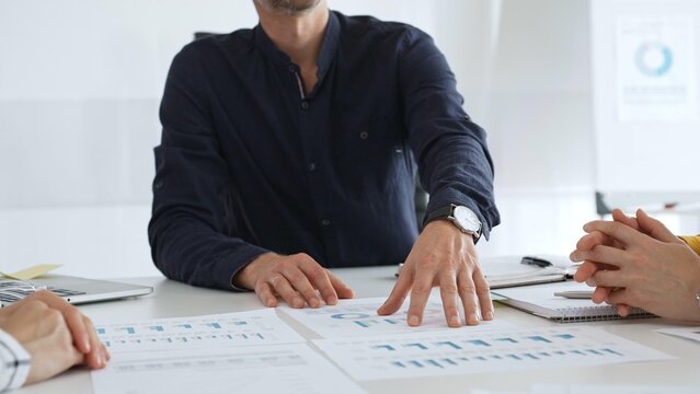 Professional colleagues reviewing financial charts, collaborating on strategic planning, gesturing toward data visualizations during corporate meeting in contemporary workspace