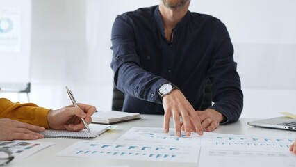 Professional colleagues reviewing financial charts, collaborating on strategic planning, gesturing toward data visualizations during corporate meeting in contemporary workspace