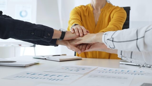 Business people team joining hands over workplace documents, symbolizing collaborative spirit and shared workplace success, close up view, casual style