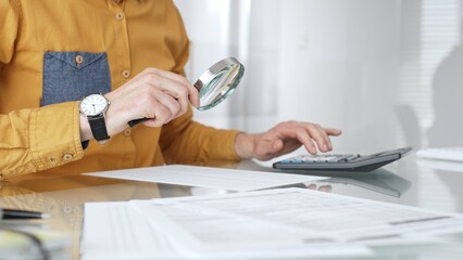 Accountant analyzing financial data with magnifying glass, calculating expenses, and auditing...